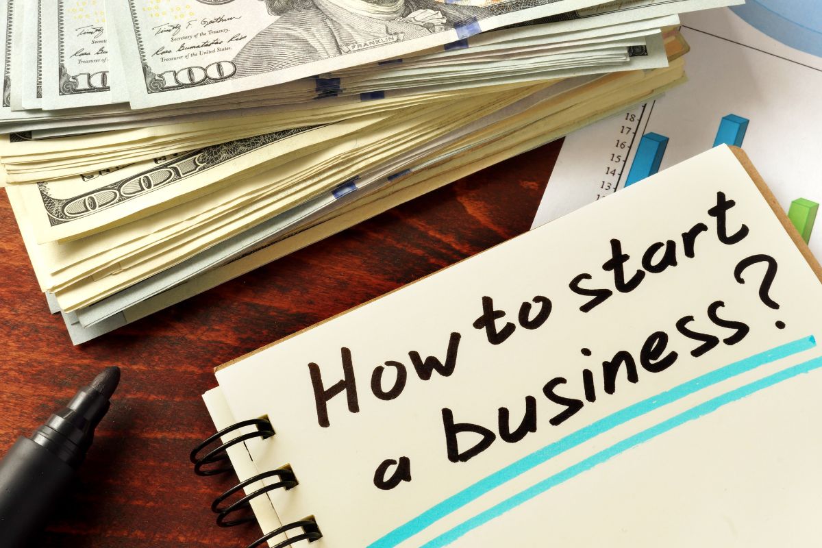 A picture showing how to start business written on a notebook and some money kept aside.