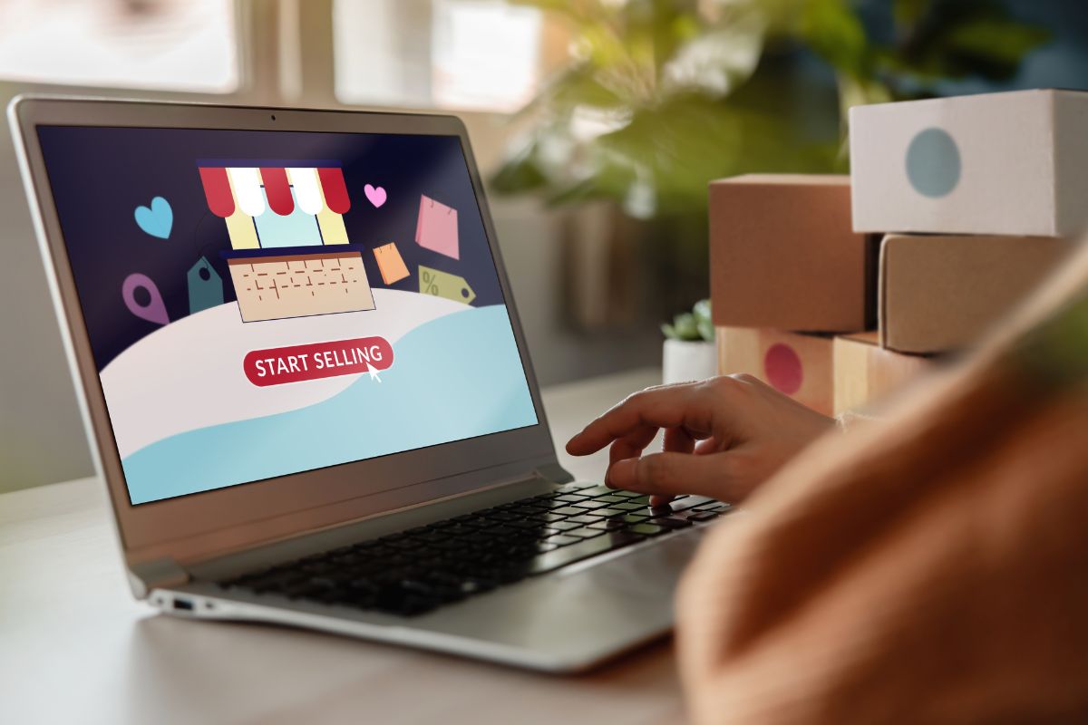 Person using a laptop on the table alongside cardboard boxes to start an etsy shop