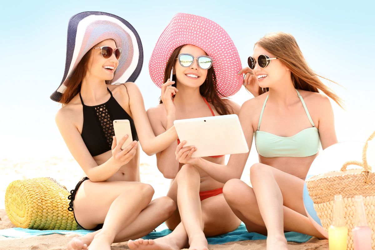 Swag women at summer beach using gadgets