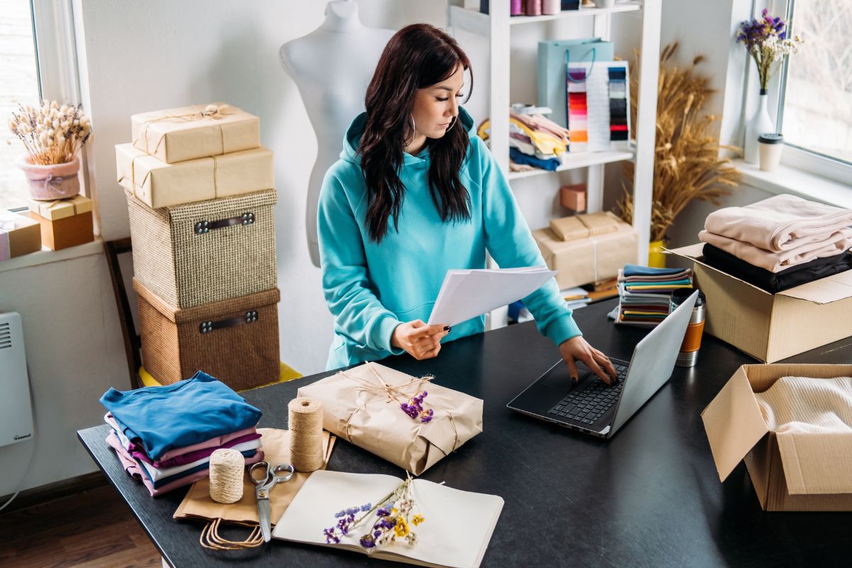 Woman with laptop and cradboard boxes on table customing swag for small business