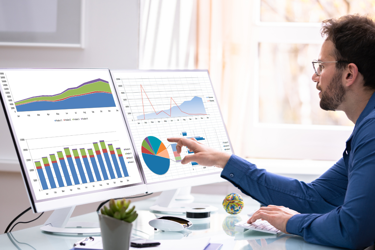 A man with two computer screens analyzing data for his print-on-demand business