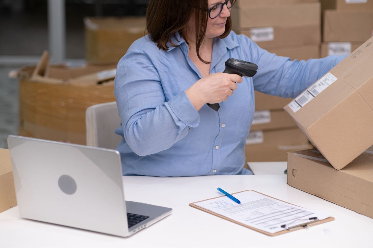A woman scanning a shipping address with a scanner while her laptop sits on the table