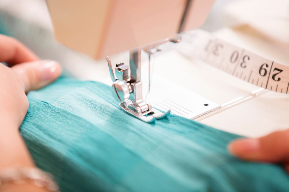 A woman stretches polyester fabric while working on sewing machine