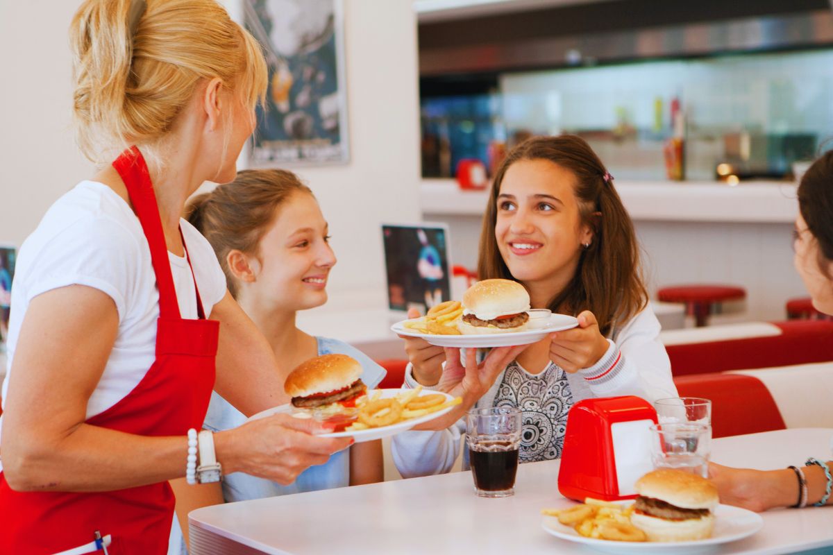 A lady wearing a restaurant t shirts and distributing food