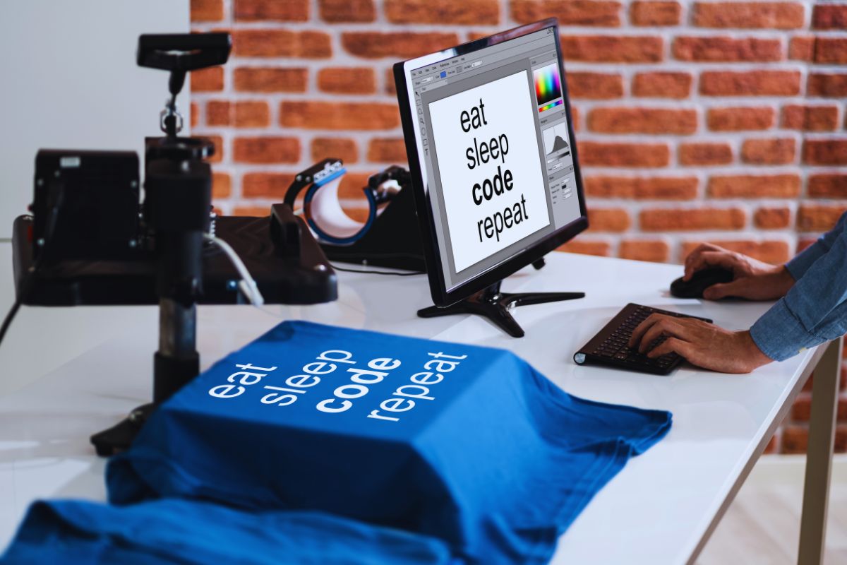 A man is printing on blue t shirt and looking at a computer