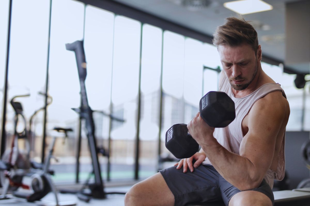 A man wearing off white muscle tank top and exercising in gym