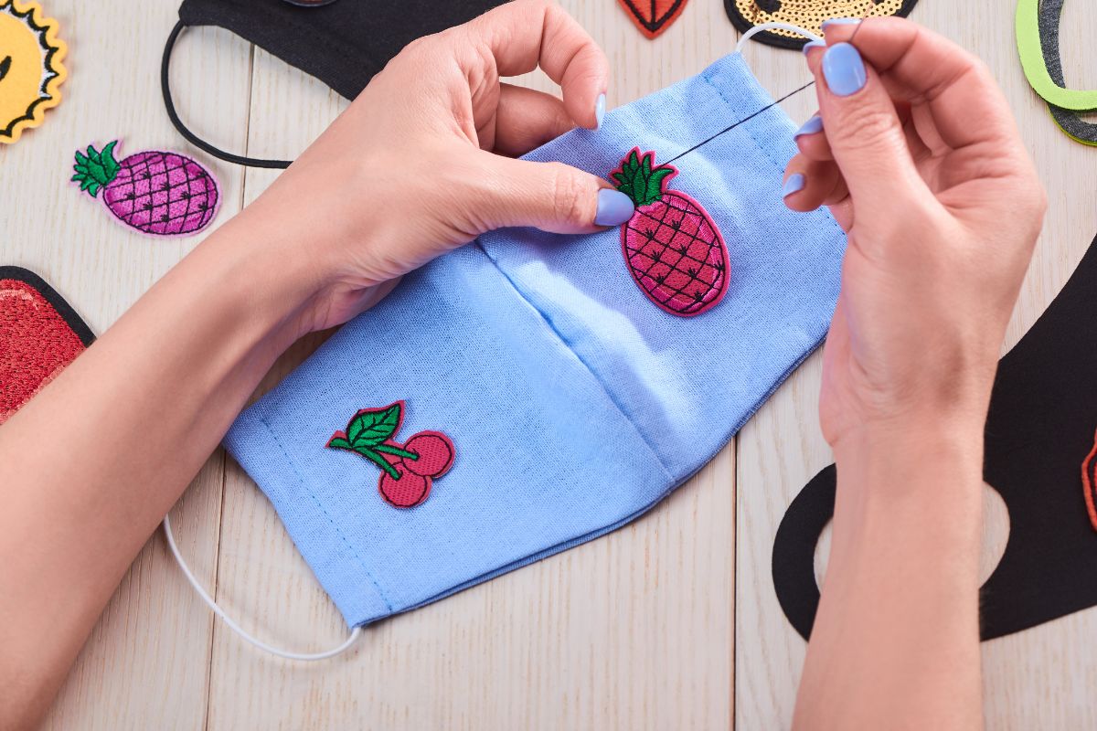 A woman is sewing a patches onto a mask.