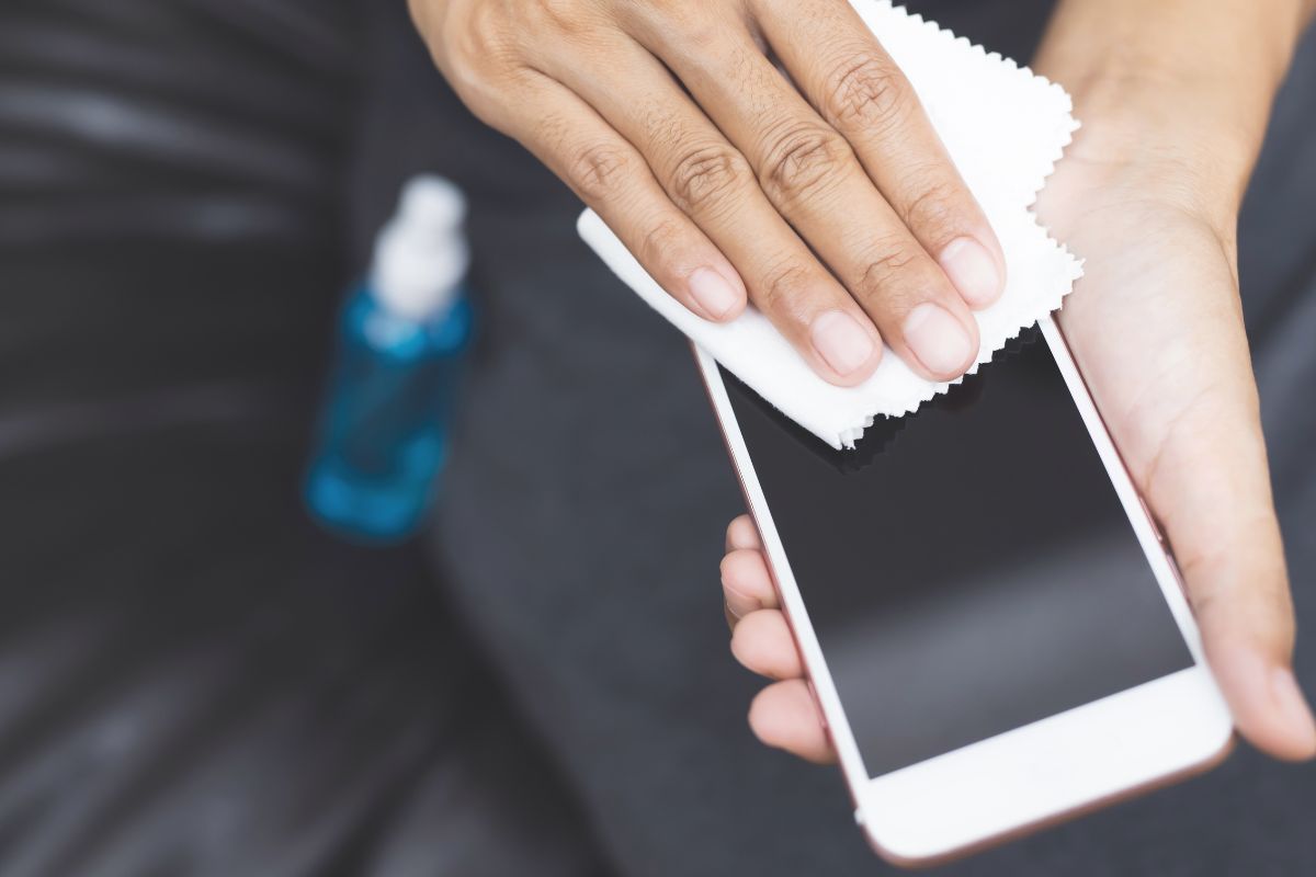 A person cleaning a mobile screen using a custom lens cleaner